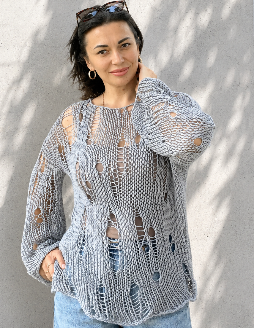 Woman wearing an oversized distressed cotton knit sweater in grey blue color with airy handmade open-knit texture and relaxed minimalist