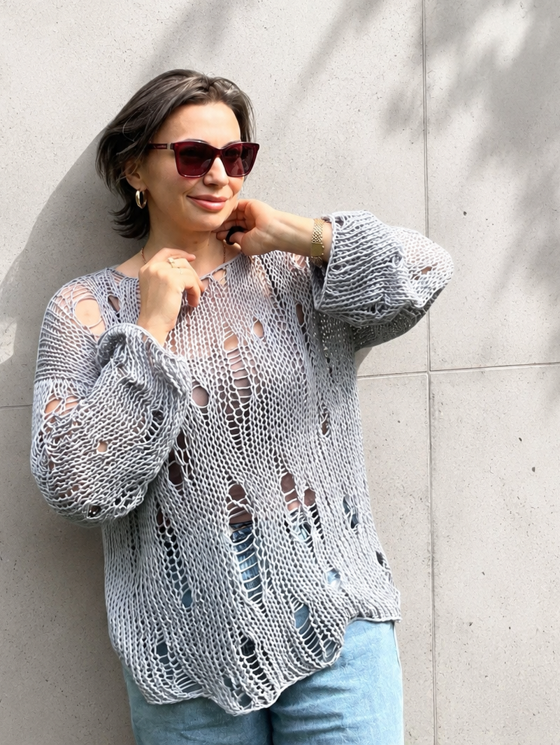 Close-up detail of an oversized distressed cotton knit sweater with airy open-knit texture and handmade relaxed summer styling